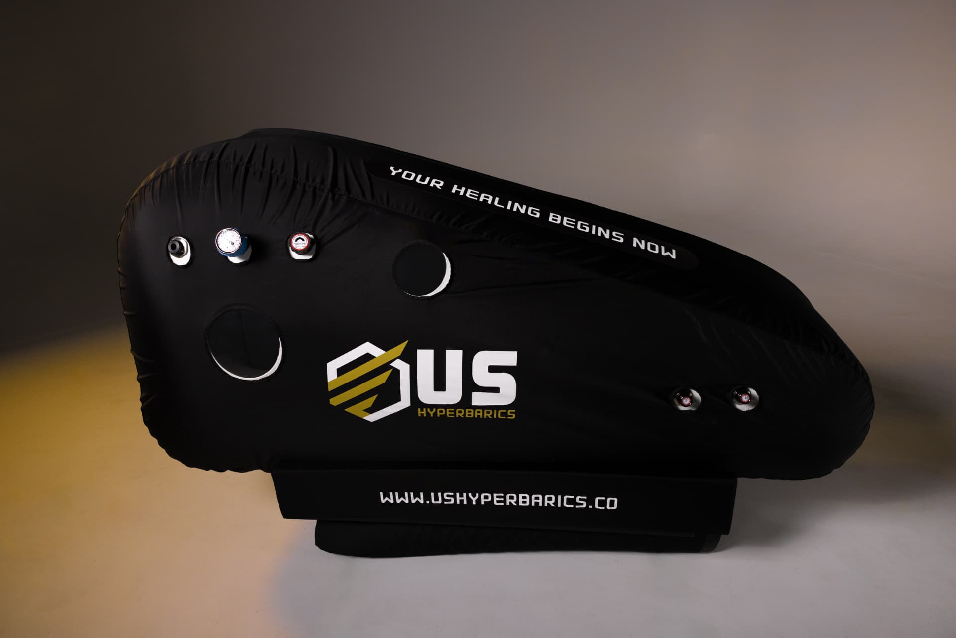 US Hyperbarics hyperbaric oxygen chamber, studio profile view with pressure gauge and Your Healing Begins Now branding